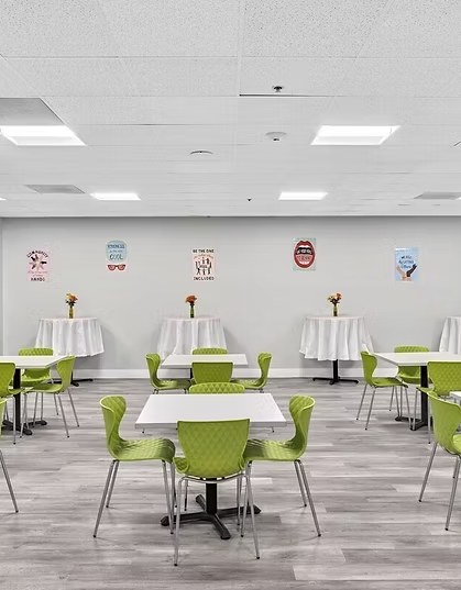 An open community room with white tables, green chairs, and encouraging posters on the wall